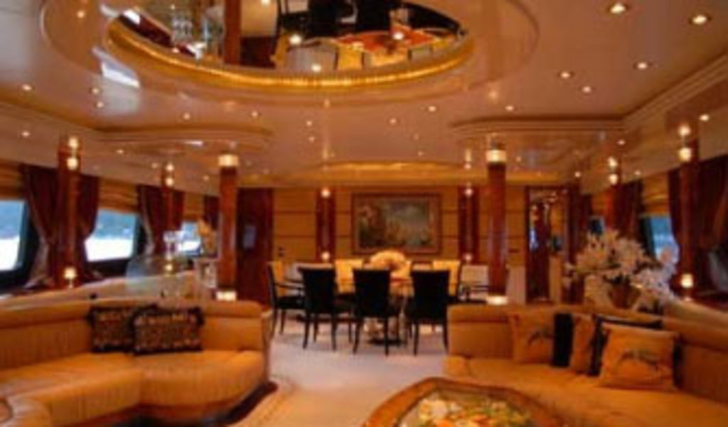 Ein Hotellobby mit Sofas, Stühlen, Tischen und Dekorationsgegenständen im Vordergrund, Fenstern mit Vorhängen und Lampen auf beiden Seiten, einem gerahmten Bild und Beleuchtung im Hintergrund und einem Spiegel mit Deckenleuchten oben.