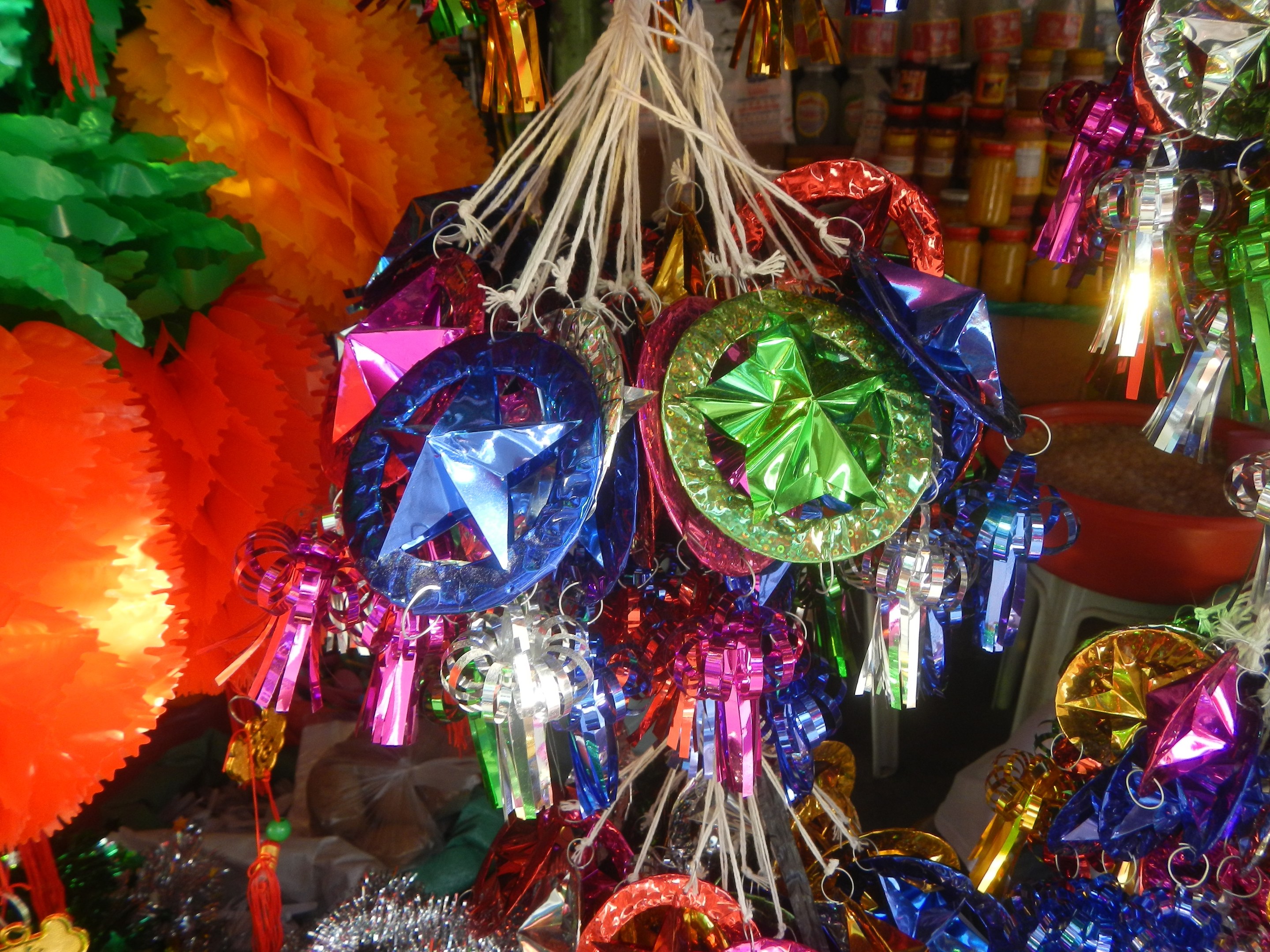 Bunte Dekorationen wie Laternen und Bänder hängen von der Decke über Regalen voller Flaschen in einer festlichen Atmosphäre.