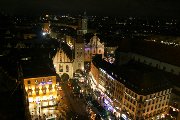 Eine Vogelperspektive einer Stadt bei Nacht, mit zahlreichen Gebäuden, Häusern, Straßen voller Fahrzeuge und Menschen.