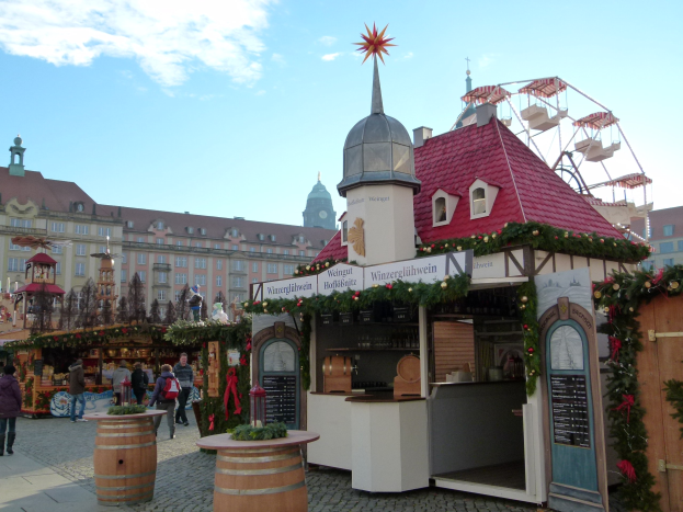 Ein geschäftiger Weihnachtsmarkt in Nürnberg, Deutschland, mit Menschen um geschmückte Buden, festliche Lichter, ein Riesenrad im Hintergrund und eine Schautafel rechts.
