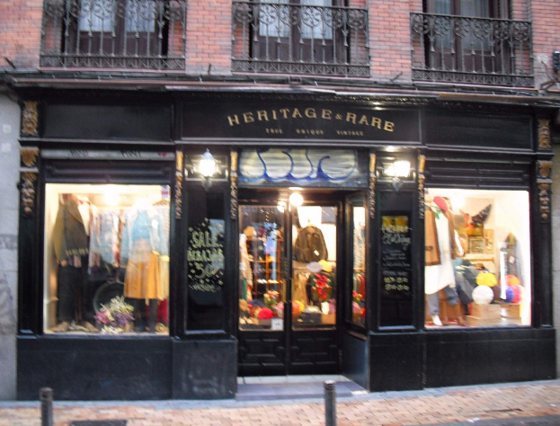 Erbschaft und rares Boutique in Madrid mit Schaufensterpuppen im Fenster, Geländern, einer Namensschild und einer Straße unten.