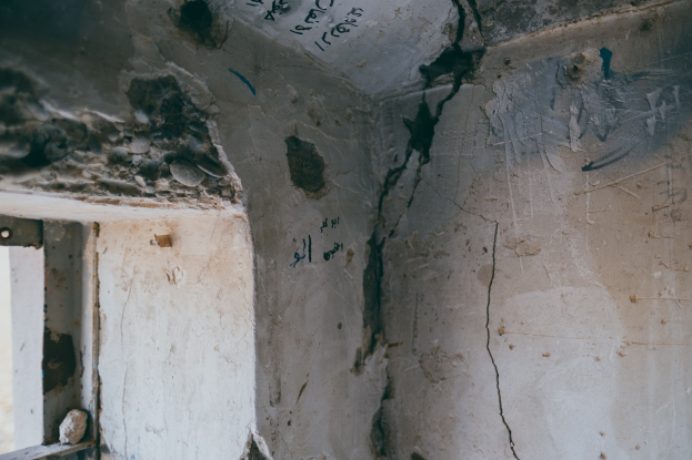 Ein Raum mit einem Fenster auf der linken Seite und einer Wand mit einem Riss, der hindurchläuft und mit Graffiti bedeckt ist.