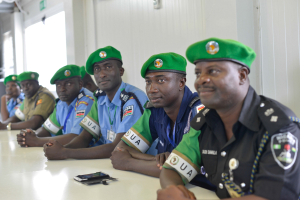 Gruppe von Polizeibeamten, die an einem Tisch während einer Schulung sitzen, mit Mobiltelefonen und anderen Gegenständen auf dem Tisch, in einem Raum mit Fenstern links und einer Wand im Hintergrund.