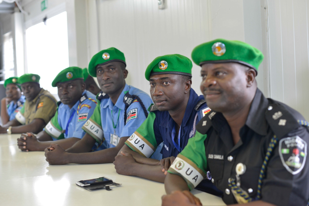 Gruppe von Polizeibeamten, die an einem Tisch während einer Schulung sitzen, mit Mobiltelefonen und anderen Gegenständen auf dem Tisch, in einem Raum mit Fenstern links und einer Wand im Hintergrund.