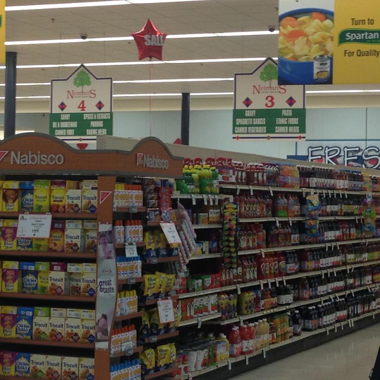 Ein Supermarkt-Innenraum mit sichtbaren Lebensmitteln, Deckenleuchten und Beschilderung.