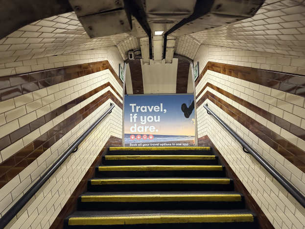 Eine Treppe in einer U-Bahn-Station mit einem "Reise, wenn du wagst"-Schild oben, flankiert von Geländern und sichtbaren Stationwänden.