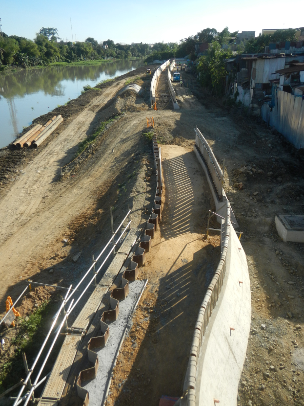 Eine Baustelle mit einem Fluss auf der linken Seite, Gebäuden und Bäumen auf der rechten Seite und einem sichtbaren Himmel oben.