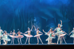Eine Gruppe von Balletttänzern in bunten Kostümen, die 'Nussknacker' auf der Bühne des Royal Opera House tanzen, sich synchronisiert gegen einen blauen Hintergrund bewegen.