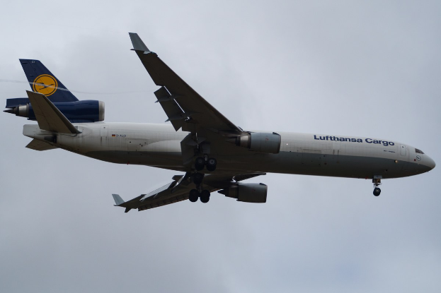 Ein Lufthansa Cargo Boeing 777-300ER im Flug, mit ausgebreiteten Flügeln und laufenden Triebwerken, mit sichtbarem Text auf dem Rumpf gegen einen wolkengefüllten Himmel.