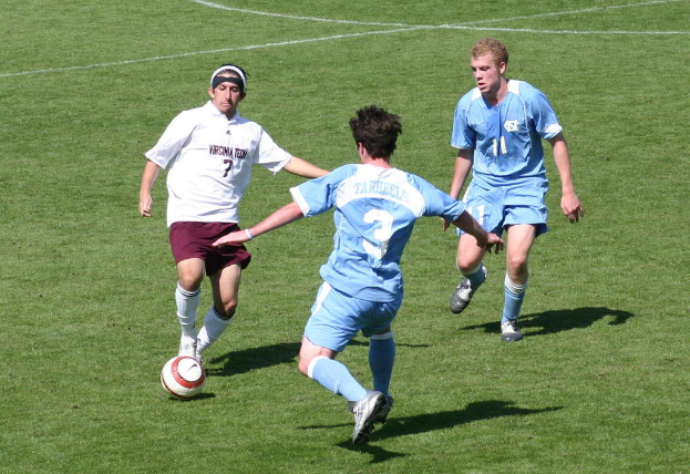 Drei Männer spielen Fußball auf einem Feld.