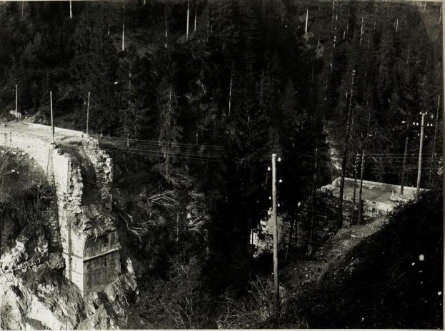 Ein Schwarz-Weiß-Foto einer Brücke über einem Fluss während ihrer 1930er-Jahre-Erstellung, mit Bäumen, Pfählen und Felsen im Hintergrund.