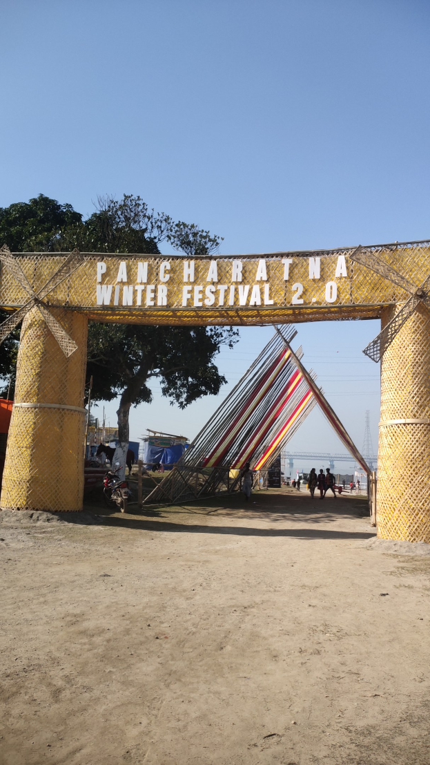 Riesenrad auf einem Festival mit einem Bogen, Menschen, Pfählen, einem Turm, Bäumen und einem bewölkten Himmel.