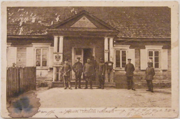 Ein Schwarz-Weiß-Foto von einer Gruppe von Männern, die vor einem Gebäude mit Fenstern, Säulen und einem Dach stehen, mit einem Zaun auf der linken Seite und einem Text unten, der 'Deutsche Post in Berlin' lautet.