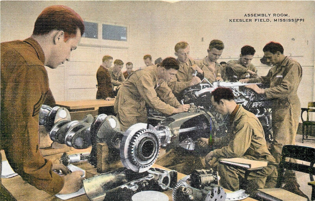 Eine Gruppe von Männern, die an einer Maschine in einem Montageräumen arbeiten, mit Tischen, Stühlen und Fenstern im Hintergrund und verschiedenen Gegenständen auf den Tischen sowie Text am unteren Bildrand.