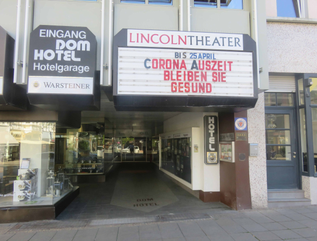 Außenansicht des Lincoln Theaters in Berlin, Deutschland, mit Glasfenstern, Türen und einer Texttafel, mit einer belebten Stadtlandschaft im Inneren sichtbar.