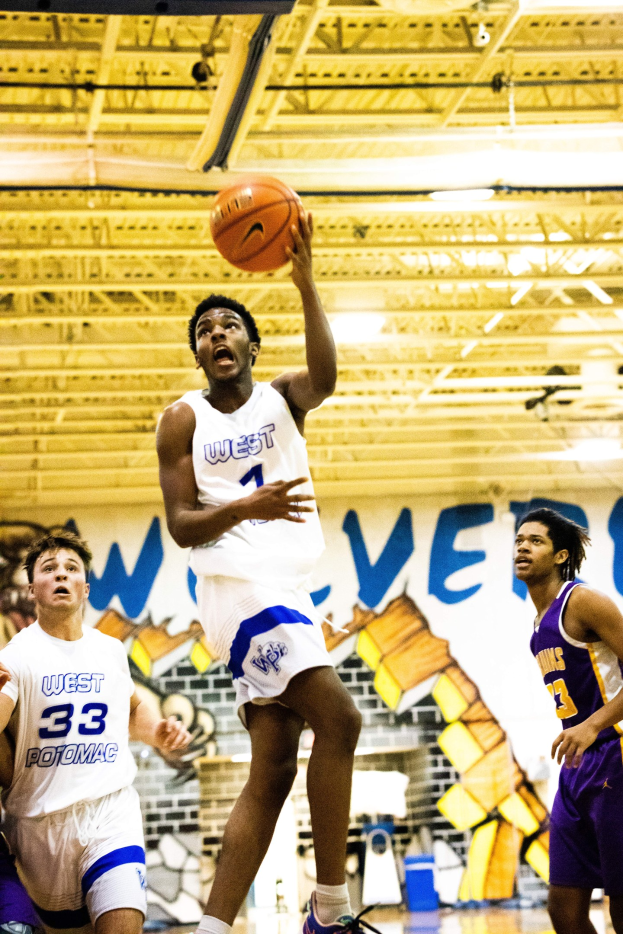 Gruppe junger Männer, die Basketball in einer Turnhalle mit einer bemalten Wand und Deckenlampen im Hintergrund spielen, ein Spieler in Turnschuhen in der Mitte.