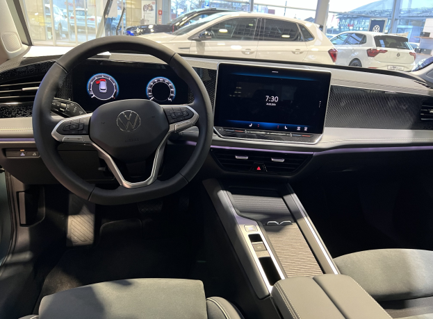 Das Innere eines Volkswagen e-Golf mit einem Lenkrad, Armaturenbrett, Bildschirmen, Knöpfen, Sitzen und Glastüren.