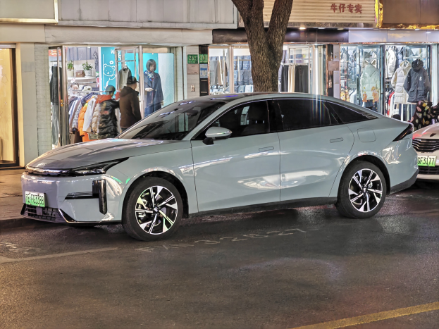 Elektrischer Mitsubishi Lancer EV auf einer nächtlichen Stadtstraße geparkt, umgeben von beleuchteten Schaufenstern, Puppen und Schildern.